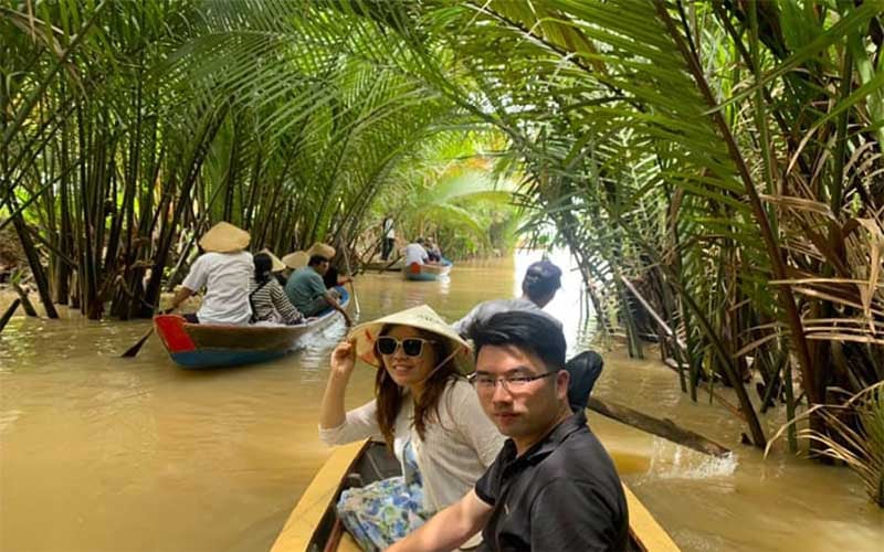 Tourists on a traditional wooden boat weaving through lush green canals in the Mekong Delta.